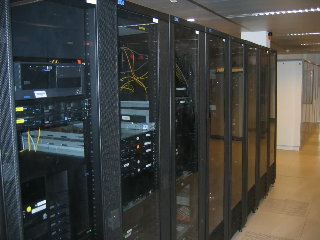 A row of black glass-fronted server racks with cabling, seen along a data centre aisle.